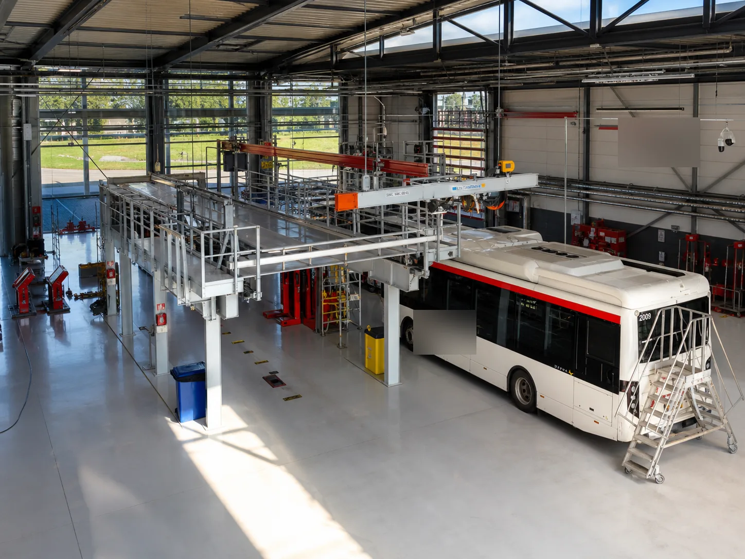 Bus in een onderhoudswerkplaats naast een dakbordes, met inspectieputten in de vloer